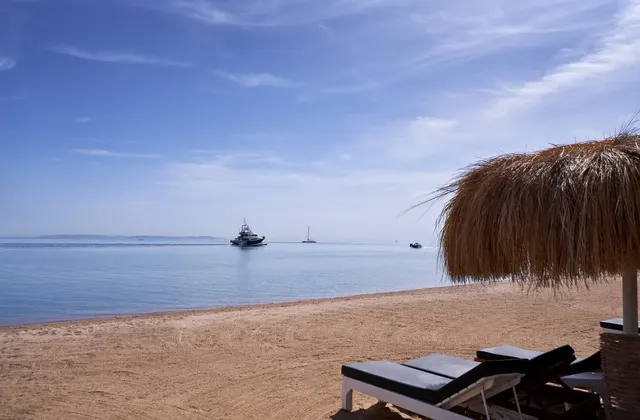 Sandy beach with a thatched umbrella in the foreground and boats anchored offshore