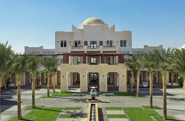 Domed main building of a resort with a palm-lined courtyard and fountain in front