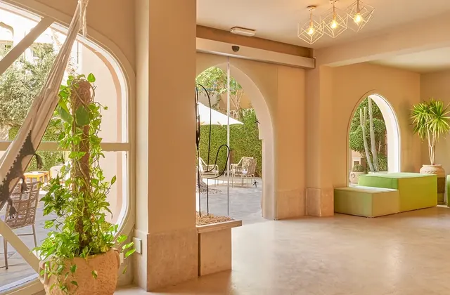 Bright hotel lobby with green seating, potted plants and arched windows opening onto a courtyard
