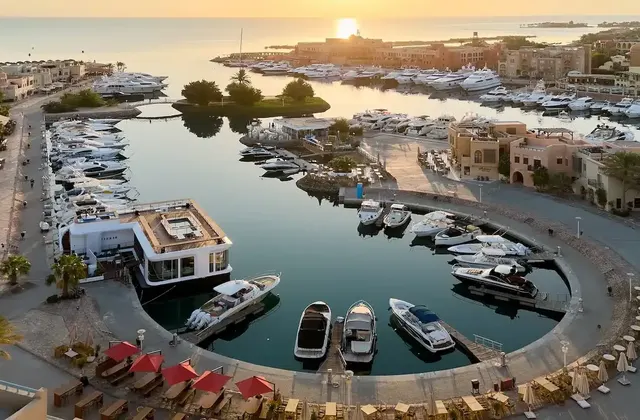 Aerial view of a marina at sunrise with yachts docked along a circular waterfront promenade