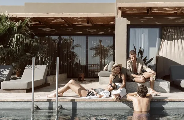 Group of friends relaxing on loungers and in the pool beside a beach-style cabana