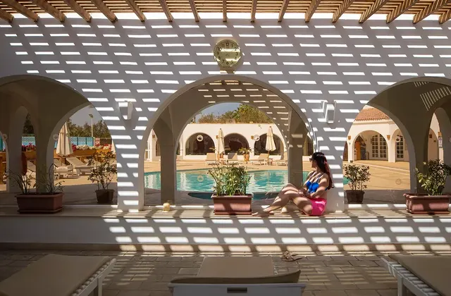 Sunlit arched walkway with a woman relaxing beside a pool seen through the arches