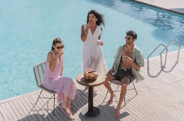 Three friends chatting around a small table beside a swimming pool