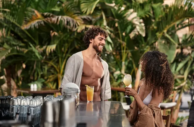 Man and woman chatting at an outdoor bar counter surrounded by tropical greenery