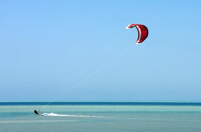 Person kite surfing on a windy day, gliding over waves in the sea with a colorful kite flying above.