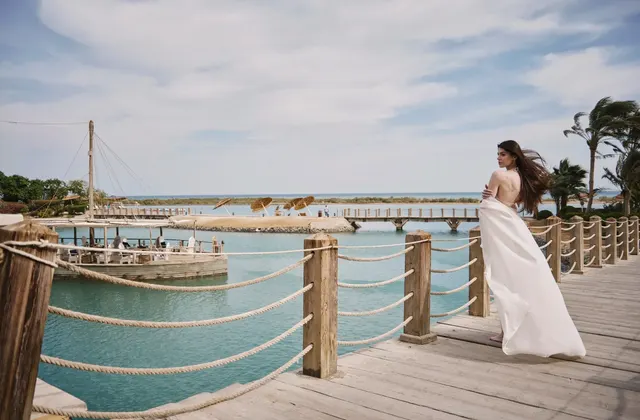 Bride in a flowing white gown standing on a rope-lined wooden pier over turquoise water