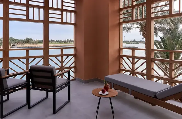 Balcony with two armchairs, a small table, and a lounger overlooking a lagoon through wooden latticework