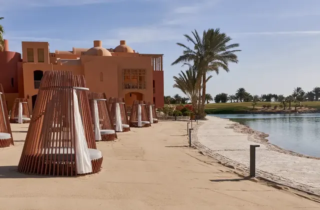 Beach path lined with cone-shaped woven cabanas and palm trees beside a lagoon