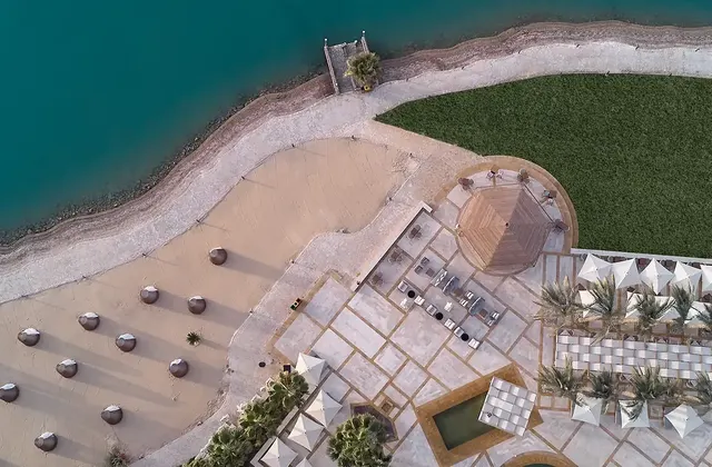 Aerial view of a resort's beachfront with lounge chairs, sunshade huts, and a pool beside the turquoise sea