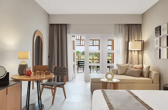 Hotel room with a king bed, seating area, and open glass doors leading to a balcony with a golf course view