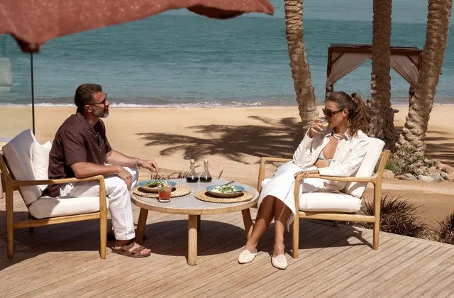 Couple relaxing on a wooden deck by the beach with drinks and snacks on a low table