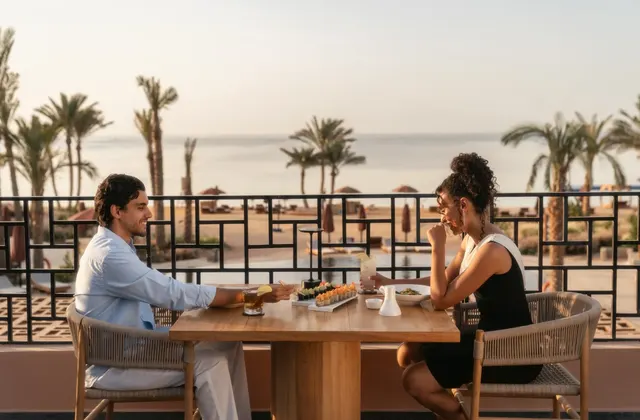 Couple dining at a terrace table at sunset with the sea and palm trees behind them