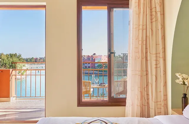 Hotel room with a king bed, sheer curtains and a window overlooking a marina and pastel-colored buildings