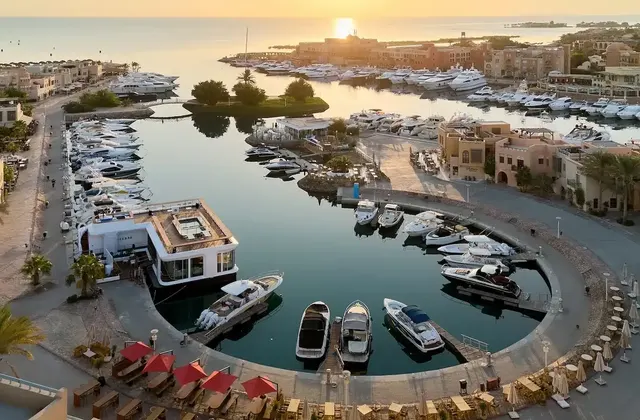 Aerial view of a marina at sunset with boats docked around a curved waterfront lined with buildings